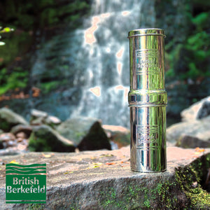 1L Adventure British Berkefeld stainless steel drinking water gravity filter shown outdoors in front of waterfall.